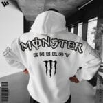 Back view of a man wearing a white oversized hoodie featuring the large Monster Energy text logo and M-claw graphic, with M-claw logos on the sleeves.