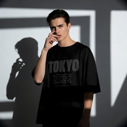 Model wearing a black oversized t-shirt with a tonal dark grey graphic print that says "TOKYO" and the Japanese Kanji "東京".
