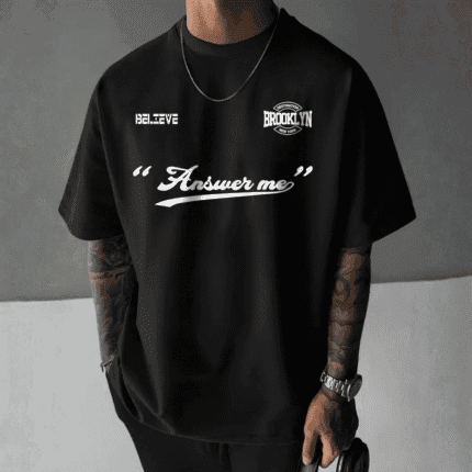 Front view of a man wearing a black oversized t-shirt with white text graphics including "BELIEVE", "DESTINATION BROOKLYN NEW YORK", and "Answer me".