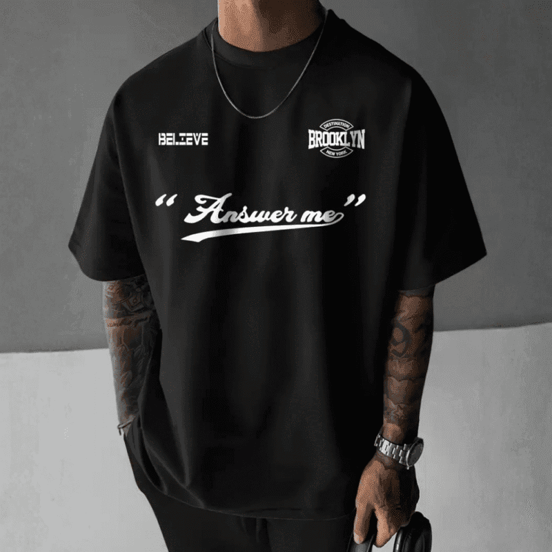 Front view of a man wearing a black oversized t-shirt with white text graphics including "BELIEVE", "DESTINATION BROOKLYN NEW YORK", and "Answer me".
