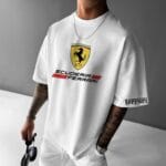 Front view of a man wearing a white oversized t-shirt with a large Scuderia Ferrari shield logo on the chest and "Ferrari" text on the left sleeve.